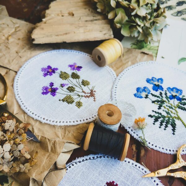 Delicate handmade floral embroidery displayed on fabric circles with sewing tools.